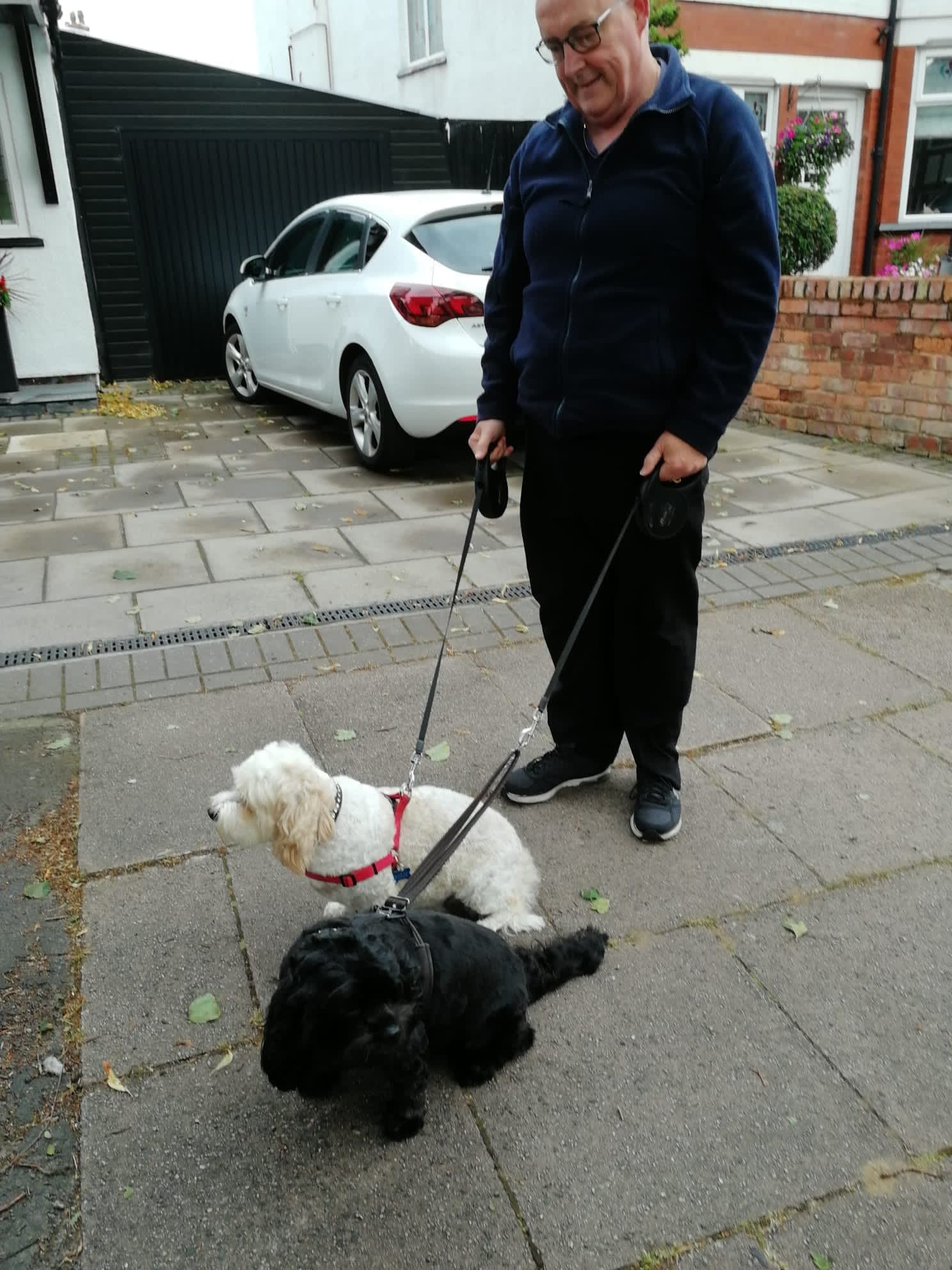 Brian in a navy jacket walking a white fluffy dog and a black cockapoo on leads along a driveway